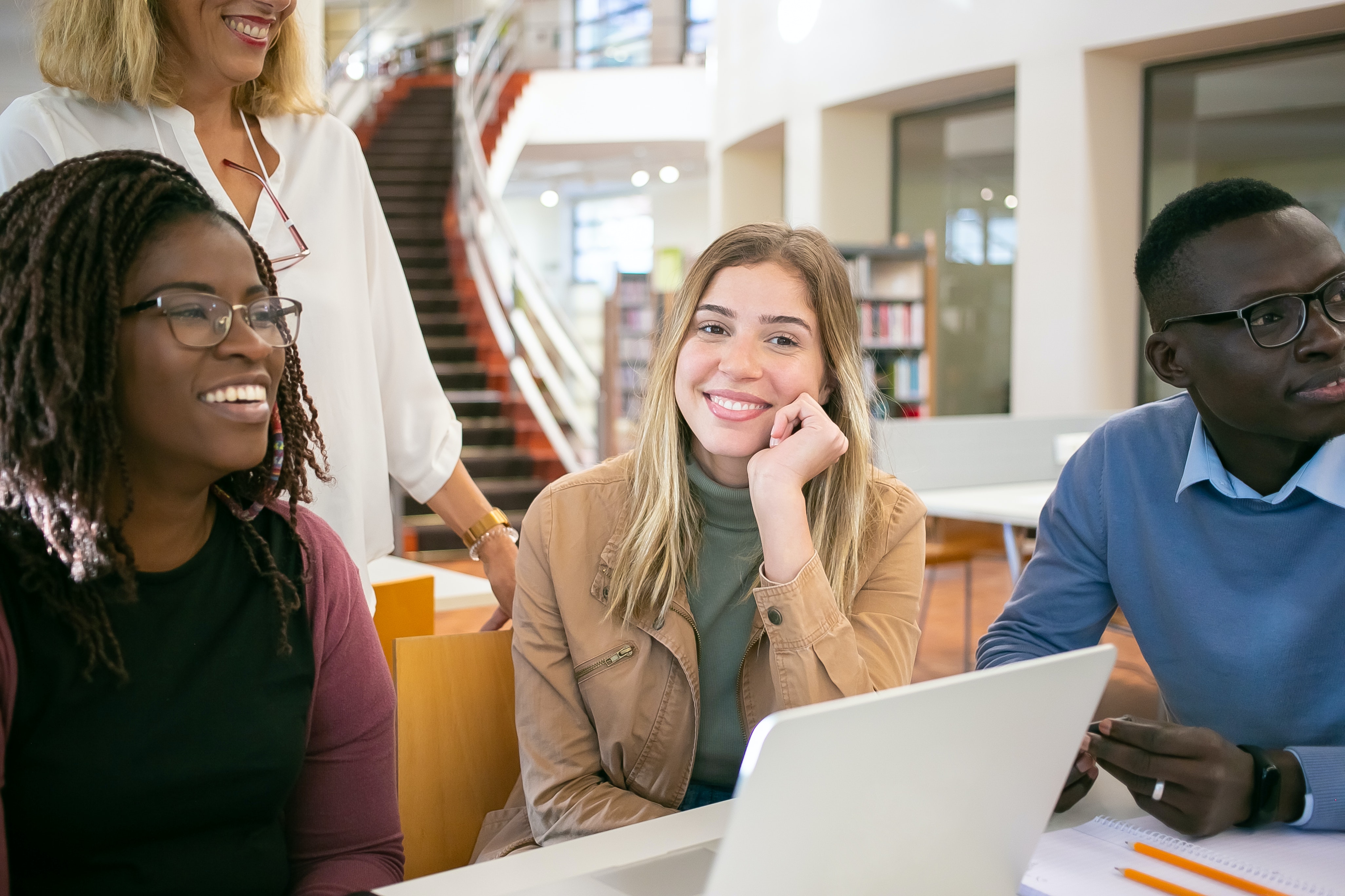 Tre studenter tillsammans med en lärare i ett bibliotek.