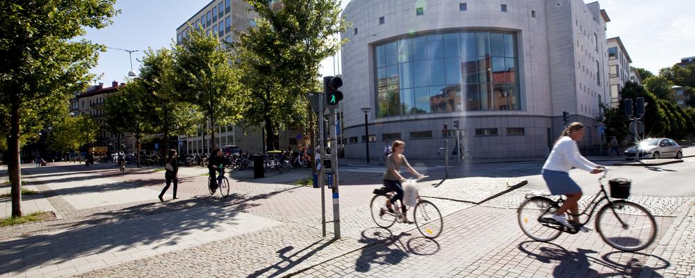 Två personer cyklar framför en byggnad.